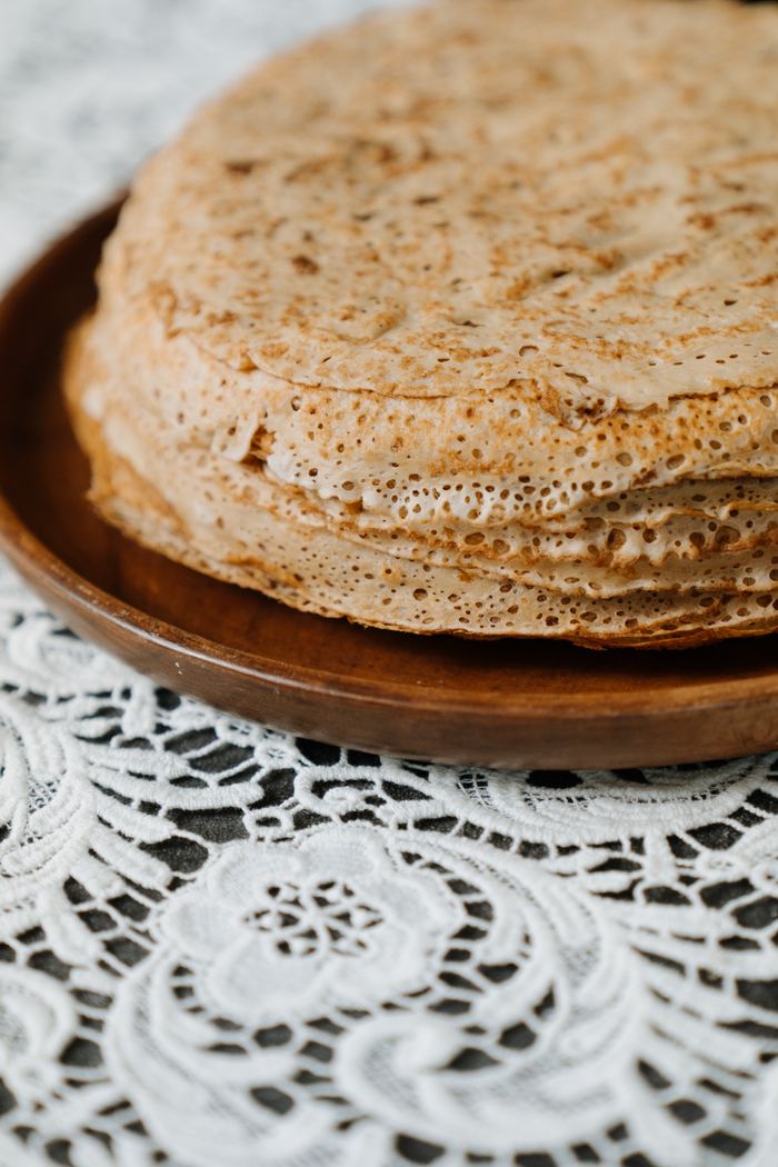 Close-up of traditional Russian blini on a wooden plate atop lace tablecloth.