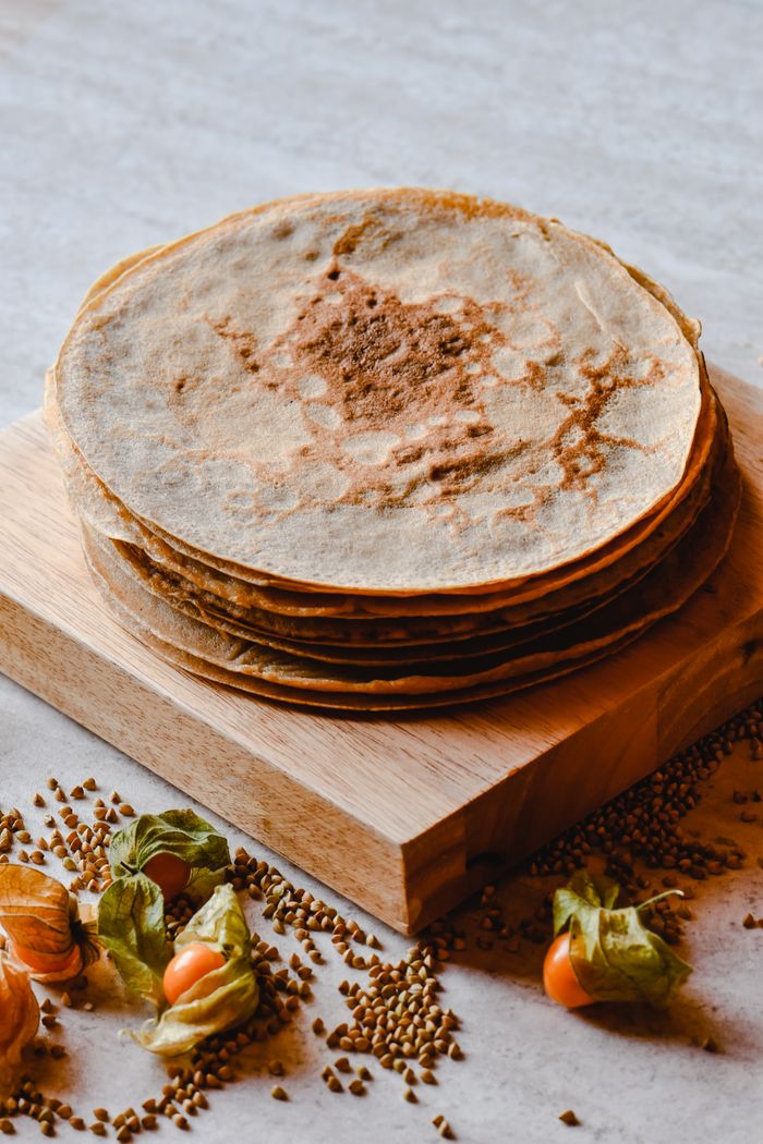 Delicious homemade buckwheat pancakes stacked beautifully, surrounded by grains and fruits, perfect for a cozy breakfast vibe.